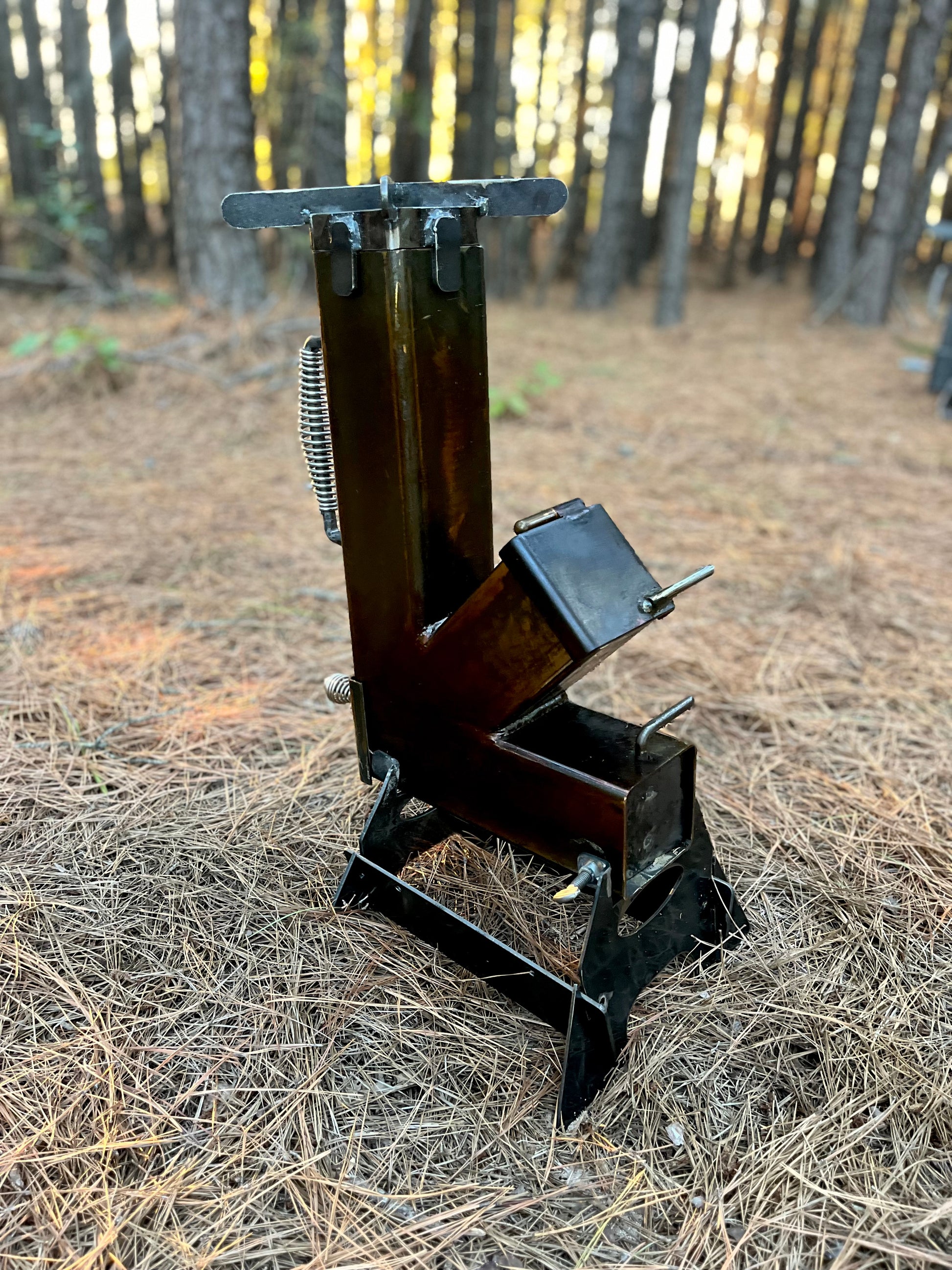 metal rocket stove on a forest floor with trees in the background camping and high heat cooking fireplace