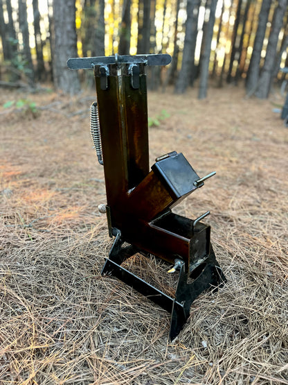 metal rocket stove on a forest floor with trees in the background camping and high heat cooking fireplace