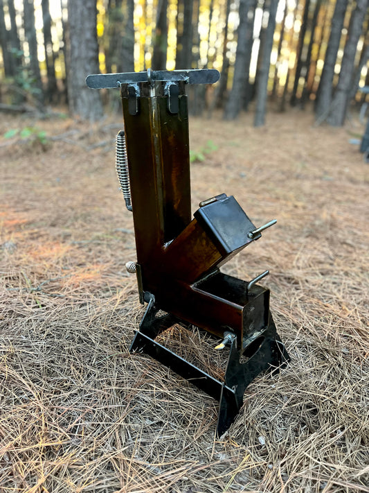 metal rocket stove on a forest floor with trees in the background camping and high heat cooking fireplace