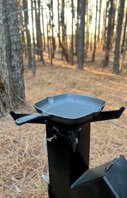 metal rocket stove on a forest floor with trees in the background camping and high heat cooking fireplace with cook cast iron skillet