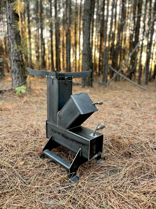 metal rocket stove on a forest floor with trees in the background camping and high heat cooking fireplace