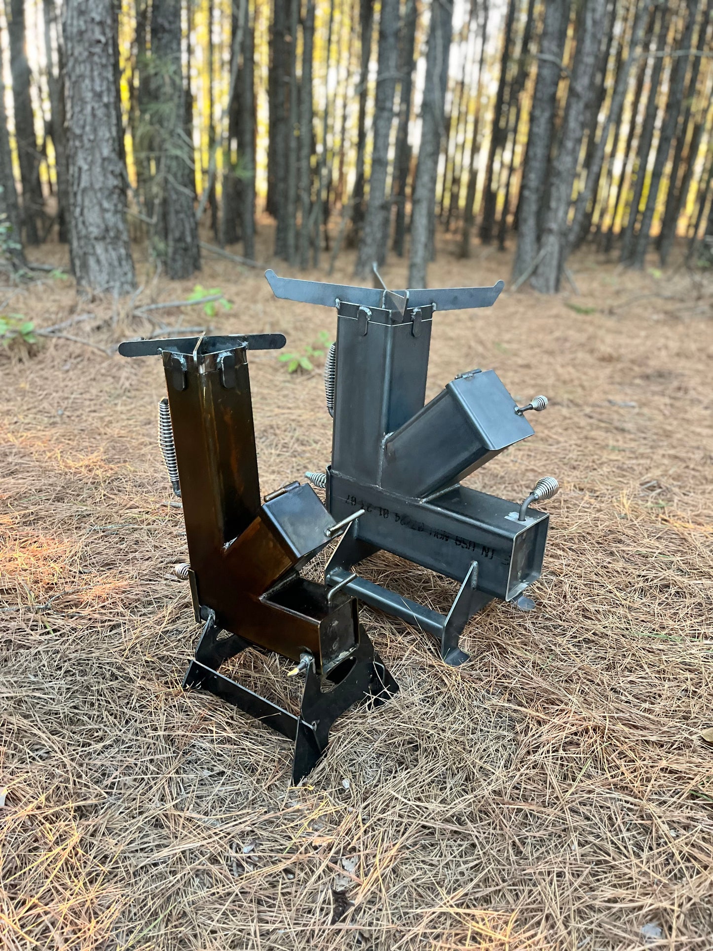 metal rocket stove on a forest floor with trees in the background camping and high heat cooking fireplace